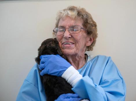 Volunteer Betty Grieb wearing a blue protective gown and gloves, holding a puppy on her shoulder