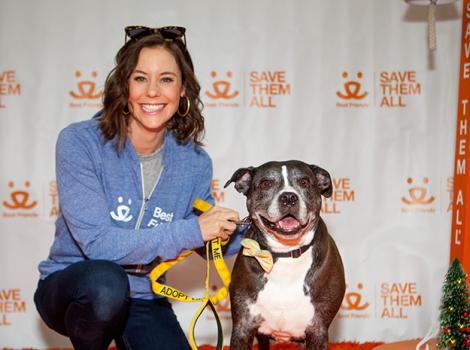 Ashley Williams in front of a Best Friends backdrop, posing with a black and white pit-bull-type dog