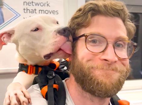 Dog in a backpack kissing the side of Bryan Reisberg's face