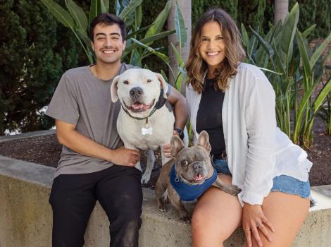 Alyssa Leon and Tommy Rigdon sitting on a ledge with Brew and Julien their adopted dogs