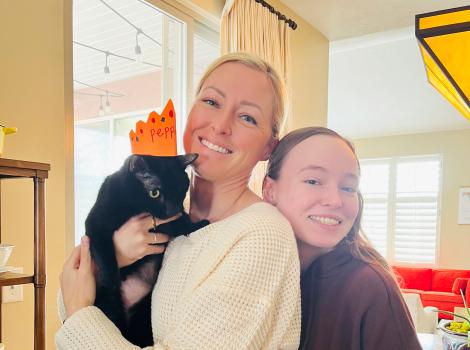 Pepper the cat wearing a crown while being held by her new family