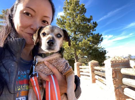 Ranko holding Soba the senior dachshund in front of a pine tree and blue sky