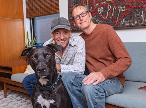 Bud the dog with his two adopters sitting on the couch behind him