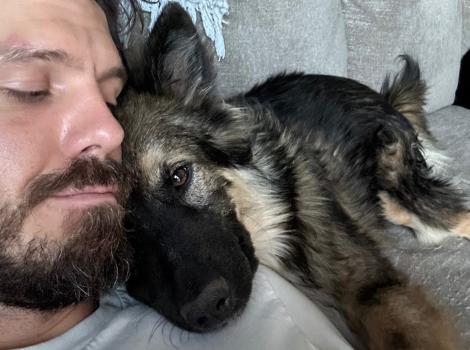 Lars the dog with his new person, lying together on a couch