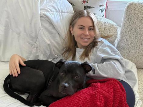 Eli the dog snuggling with Makenna Carew on a bed