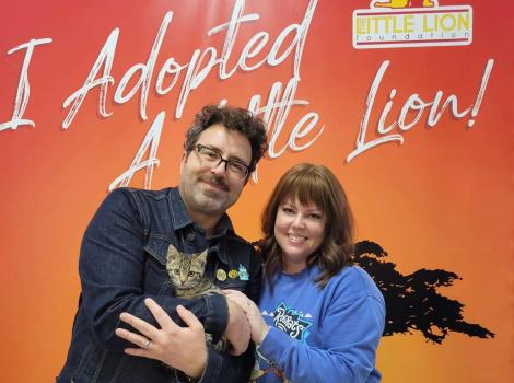 Couple adopting a kitten from Little Lion Foundation in front of a backdrop that says I adopted a Little Lion
