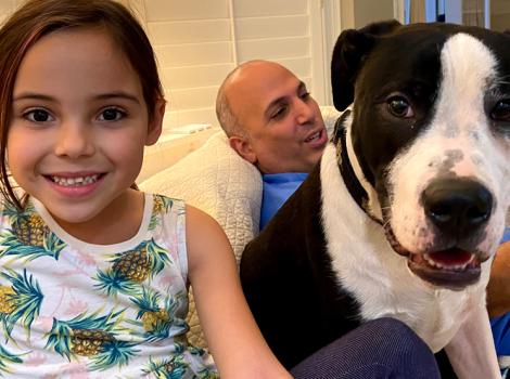 Child smiling and sitting next to black and white dog, with person behind them