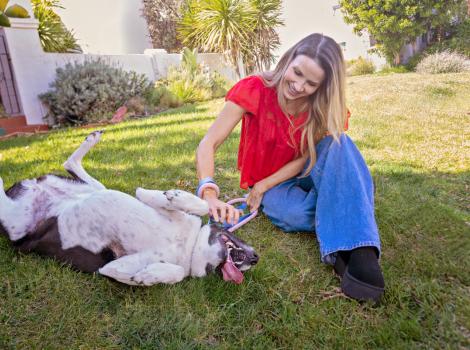 Frankie Giblin sitting on the grass beside a dog who is laying on her back