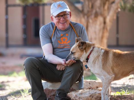 Volunteer wearing a Best Friends T-shirt sitting down and hand-feeding a treat to a dog