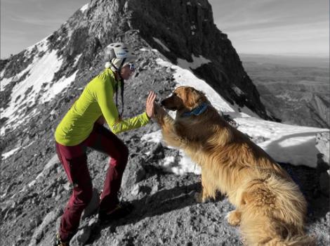 Emily and a dog doing a high-five with a mountain peak behind them
