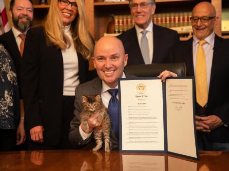 The governor of Utah, Gov. Spencer Cox, holding the written declaration as well as a kitten with Best Friends CEO Julie Castle behind him