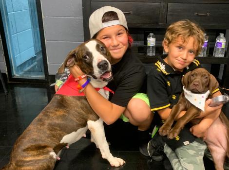 Two children associated with Grant Parish snuggling with a dog and puppy, both dogs wearing bandannas