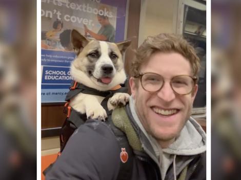 Bryan Reisberg smiling while carrying a dog in a backpack
