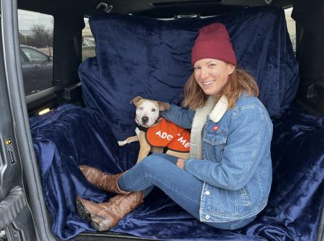Jessie the dog wearing an Adopt Me vest, in the back of a vehicle with Pam