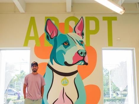 Jonathan Ramirez next to his mural of a dog with the word, Adopt