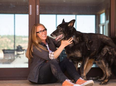 Best Friends CEO Julie Castle with her dog Shadow in front of a large window
