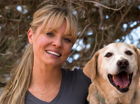 Kaitlin Doubleday wearing a Save Them All T-shirt and hugging a yellow Labrador retriever dog