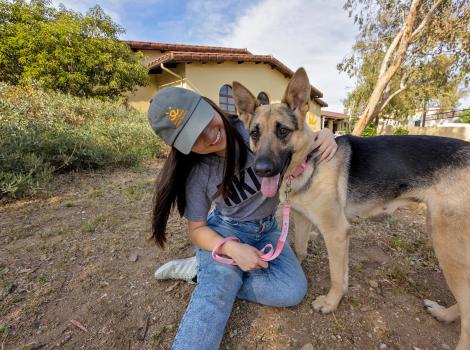 Person wearing Best Friends hat, hugging a German shepherd, by the Mission Hills location