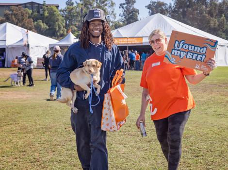 Person carrying a puppy beside a Best Friends volunteer holding a sign that says, 'I found my BFF'