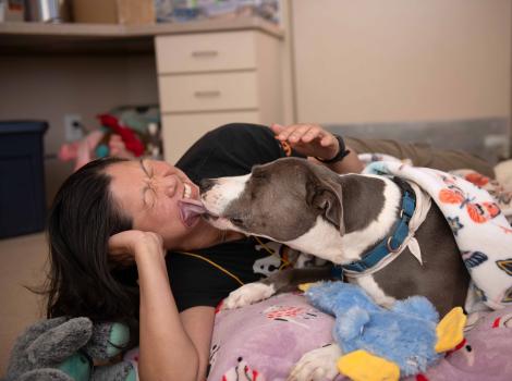 Liz Tran lying beside Sage the dog, who is licking her face