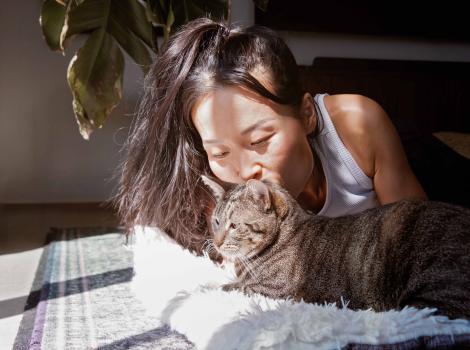 Person lying on the floor kissing the head of a brown tabby cat