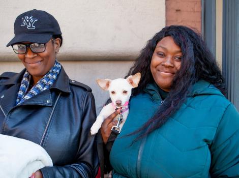 Two smiling people holding a small white dog