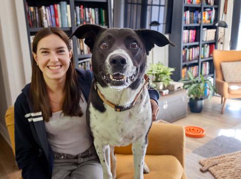 Black and white dog with the person fostering her in a home in front of bookshelves
