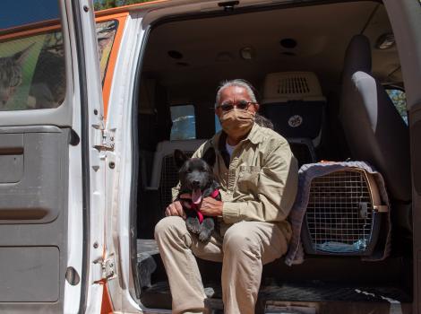Keith Slim-Tolagai with a dog on his lap, sitting in the open door of a transport van