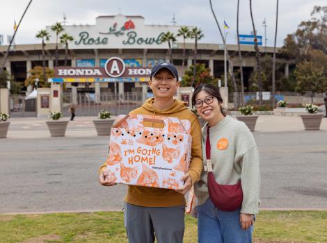 Couple holding a cat carrier containing the cat they adopted in front of the Rose Bowl