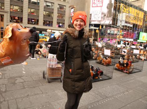 Smiling person wearing an orange Best Friends hat holding a dog balloon in Times Square