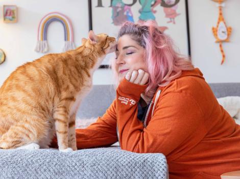 Orange tabby cat licking the forehead of a person wearing an orange hoodie
