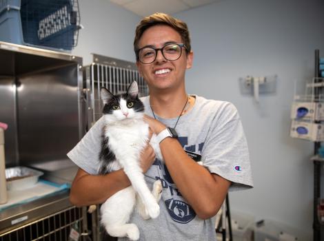 Volunteer Ben Richards holding a black and white cat in front of some kennels