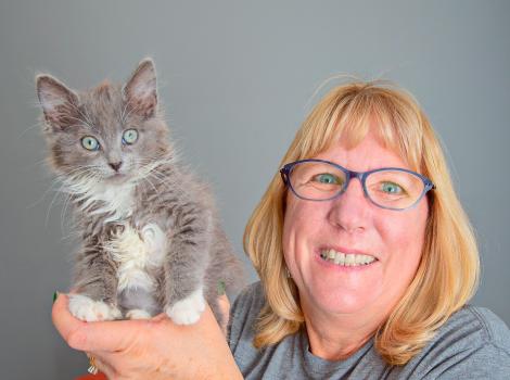 Volunteer Cheryl Baker smiling and holding a gray and white kitten