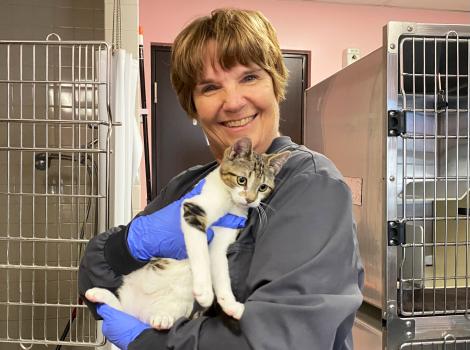 Volunteer Heather Mahood holding a tabby and white cat in front of kennels
