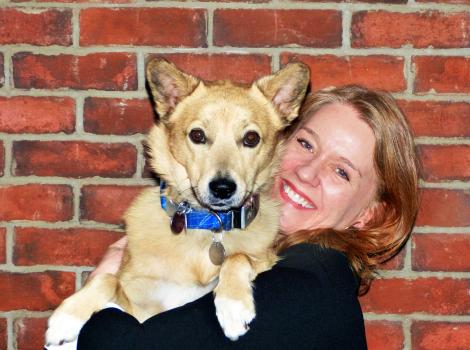 Smiling volunteer Vicki Williams holding Sunny her dog in front of a brick wall background