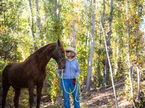 Volunteer Karin Hamilton walking Curly Sue the horse in some woods