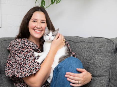Smiling person sitting on a couch while holding a cat