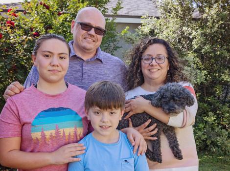 Zoey the senior dog with her new adopted family, outside in front of some bushes