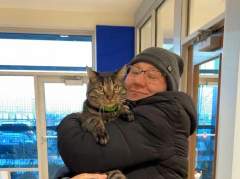 Smiling person wearing winter clothing happily hugging a tabby cat