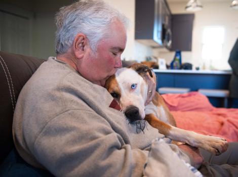Person snuggling and kissing the top of the head of a dog lying on his hap